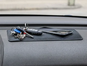 Car dashboard sticky mat holding phone and sunglasses.